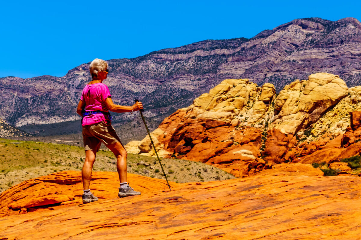 An active adult hiker pauses on vibrant orange rock formations in a sunlit desert landscape, capturing the essence of adventurous active adult living.