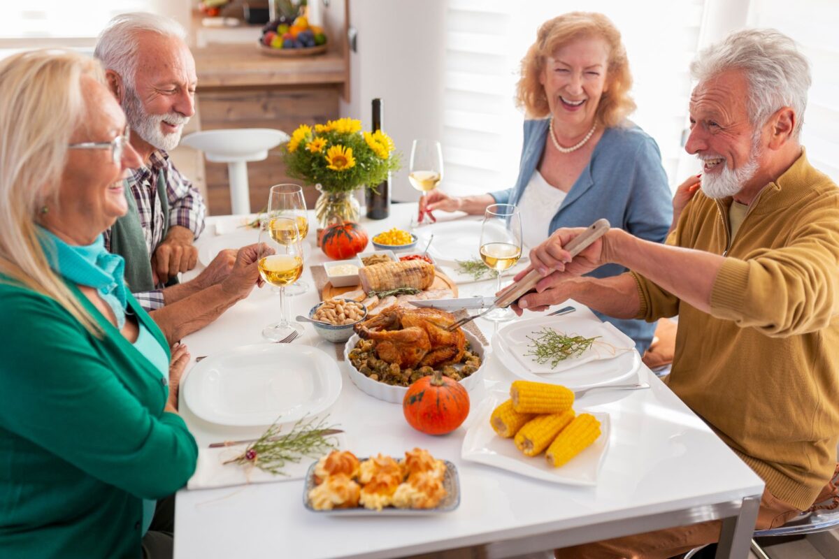 Older adults enjoying holiday hosting in senior communities with a festive meal, turkey, and wine at a beautifully decorated dining table.