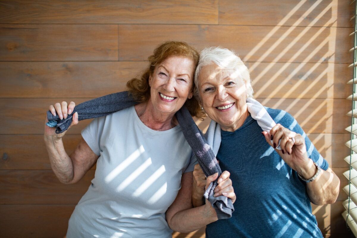 Two smiling older women with towels around their necks after exercise, enjoying friendship and wellness in an active retirement living community.