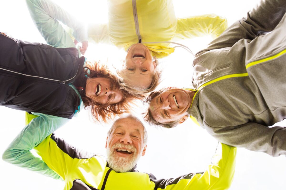 Spring in Las Vegas as four active adults stand in a circle outdoors, smiling and laughing together in bright athletic jackets under clear blue skies.